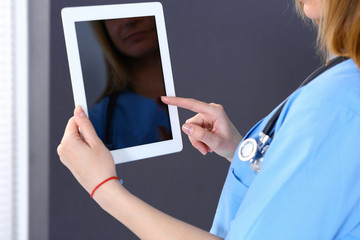 Woman doctor using tablet computer while standing straight in hospital office, closeup. Healthcare,...