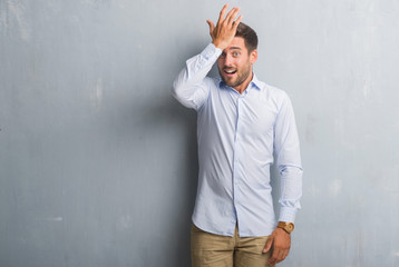 Handsome young business man over grey grunge wall wearing elegant shirt surprised with hand on head for mistake, remember error. Forgot, bad memory concept.