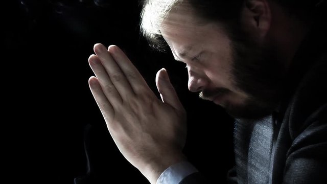 Close up profile shot of a business man in prayer. Backlit low key shot over black. Soft rays of light and smoke for enhancement.