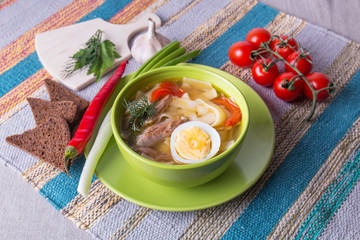 Domestic chicken noodle soup with fresh vegetables and egg. Served with bread, green onions, pepper and tomatoes