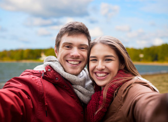 Fototapeta premium love, relationships and people concept - happy smiling young couple taking selfie over autumn beach background