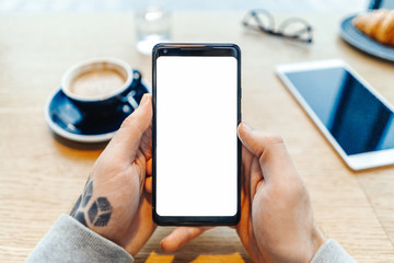 Close up of man tattooed hands holding mobile phone with blank screen.