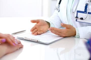 Fototapeta premium Doctor and patient talking while sitting at the desk in hospital office, close-up of human hands. Medicine and health care concept