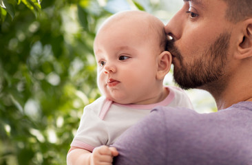 family, parenthood and people concept - close up of father kissing little baby daughter over green natural background