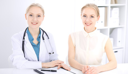 Blonde female doctor and patient talking in hospital office. Health care and client service in medicine