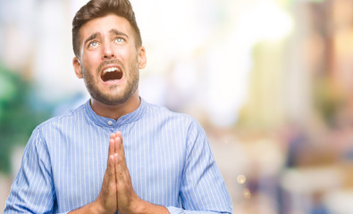 Naklejka premium Young handsome man over isolated background begging and praying with hands together with hope expression on face very emotional and worried. Asking for forgiveness. Religion concept.