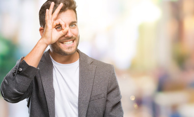 Obraz premium Young handsome business man over isolated background doing ok gesture with hand smiling, eye looking through fingers with happy face.
