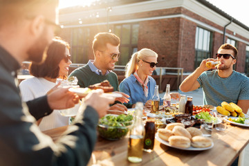 leisure and people concept - happy friends eating and drinking at barbecue party on rooftop