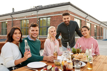 leisure and people concept - happy friends with drinks having barbecue or dinner party on rooftop