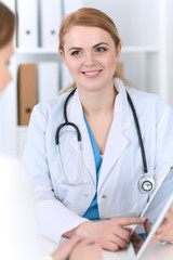 Doctor and patient using tablet pc while discussing medication history at hospital office, focus on smiling physician. Good news in medicine, health care, physical  or healthy lifestyle concept