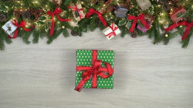 Overhead hands putting gift box.Decoration frame on light wood background with pine cones,red ribbons,blinking lights.Text or logo copy space.Vertical top view.Xmas holiday season social card.4k video