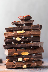 Chocolate tower. Dark and milk chocolate bars with nuts, berries and coffee beans on a grey background