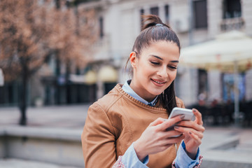 Fototapeta premium Close-up portrait of beautiful young woman using smart phone outdoor.