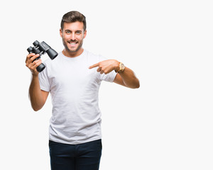 Fototapeta na wymiar Young handsome man looking through binoculars over isolated background with surprise face pointing finger to himself