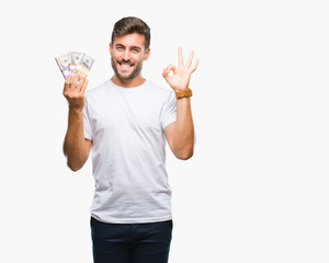 Young handsome man holding stack of dollars over isolated background doing ok sign with fingers, excellent symbol