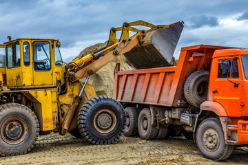 excavator loads truck in sand quarry, rain clouds in background