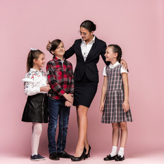 Obraz premium Cute smiling happy stylish children and female teacher on pink background. Beautiful stylish teen girls and boy standing together and posing at studio. Classic style. Kids fashion and emotions concept
