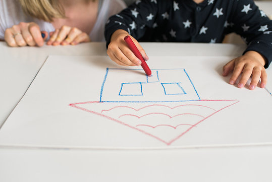 Real estate concept. Mom and kid drawing a house on a blank paper with crayons.  