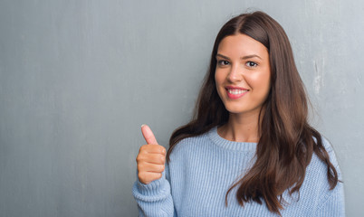 Young brunette woman over grunge grey wall happy with big smile doing ok sign, thumb up with fingers, excellent sign