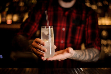 Barman holding elegant long drink glass filled with Tom Collins cocktail