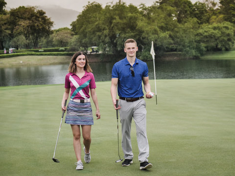 Happy golfer couple walking on green field.