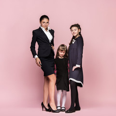 Cute smiling happy stylish children and female teacher on pink background. Beautiful stylish teen girls standing together and posing at studio. Classic style. Kids fashion and emotions concept.