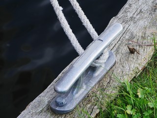Mooring cleat made of light alloy aluminum mounted on a wooden beam at a yetty for boats, a rope is...