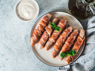 Ready-to-eat pigs sausages wrapped in bacon on plate. Fried savory sausages wrapped in bacon served...