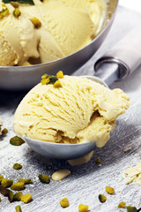 Pistachio ice cream scoop with chopped nuts and white chocolate on a rustic background.