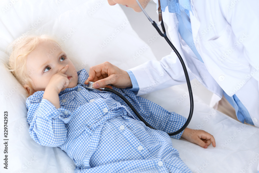 Wall mural doctor examining a little blonde girl with stethoscope.medicine and healthcare concept