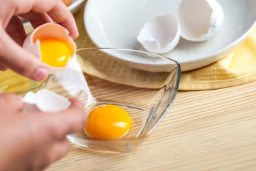 Woman hands breaking an egg to separate egg white and yolks, egg shells at the background