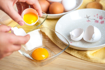 Woman hands breaking an egg to separate egg white and yolks, egg shells at the background