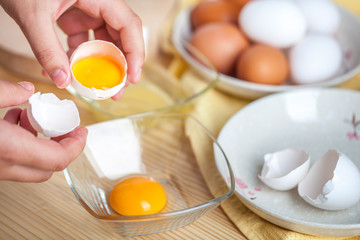 Woman hands breaking an egg to separate egg white and yolks, egg shells at the background