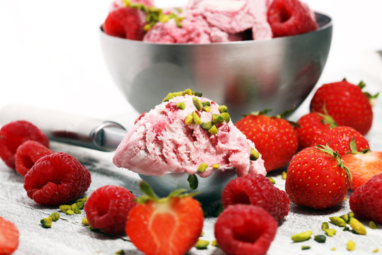 Strawberry and raspberry ice cream scoop with chopped nuts and white chocolate on a rustic background