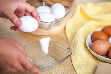 Woman hands breaking an egg to separate egg white and yolks, egg shells at the background