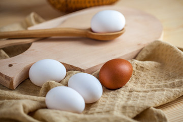 white and brown eggs on a wooden table, a towel and a wooden spoon