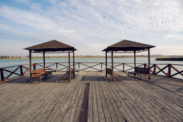two gazebos with benches standing on the pier near the lake