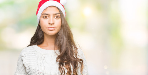 Young arab woman wearing christmas hat over isolated background with serious expression on face. Simple and natural looking at the camera.