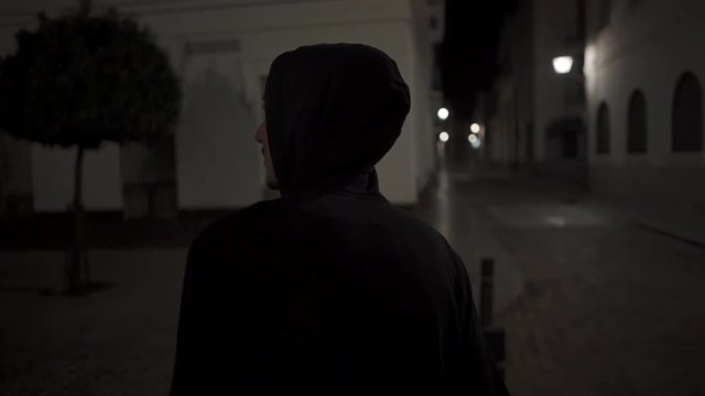 Back of a hooded young man walking down the street at night