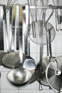 Various kitchen utensils hanging against a tiled wall in a kitchen