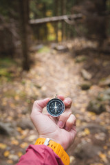 A beautiful male hand with a yellow watch strap holds a magnetic compass in the coniferous autumn forest. The concept of finding yourself the way and truth
