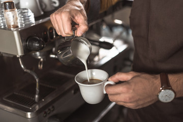 cropped shot of barista pouring milk into coffee while preparing it in restaurant