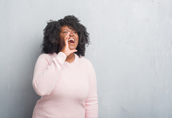 Young african american plus size woman over grey grunge wall wearing winter sweater shouting and screaming loud to side with hand on mouth. Communication concept.