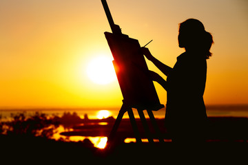 silhouette of a woman painting a picture with paints on canvas on an easel, girl with paint brush...