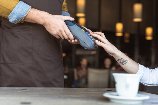 cropped shot of waiter holding payment terminal while client entering pin in cafe
