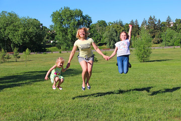 Obraz premium Happy mother having fun jumping with her daughters on green grass