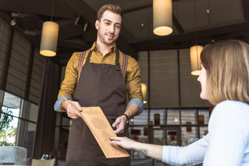 handsome young waiter showing menu list to female customer in cafe