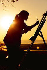 silhouette of a woman painting a picture with paints on canvas on an easel, girl with paint brush...