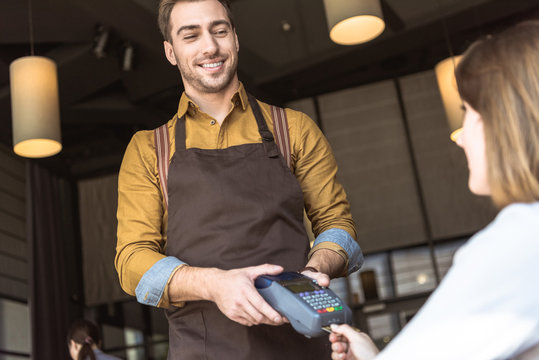 happy young waiter holding payment terminal while client inserting credit card