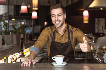 handsome young barista with cup of delicious coffee showing thumb up